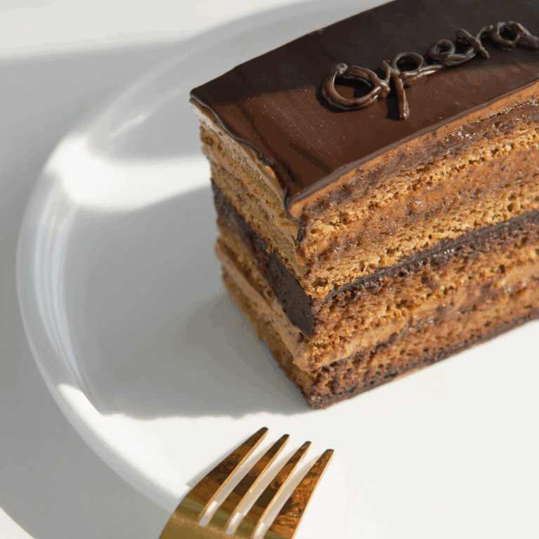 opera cake Delicious layered chocolate cake on a white plate, featuring rich chocolate ganache and intricate frosting, perfect for cake decorating and baking supplies from Over the Top Cake Supplies.