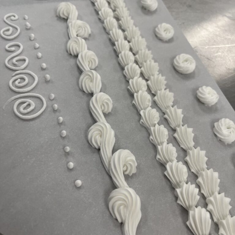 Delicate white piping gel and royal icing for cake decorating, showcasing intricate piping designs, shell motifs, and decorative borders for a professional cake finish.